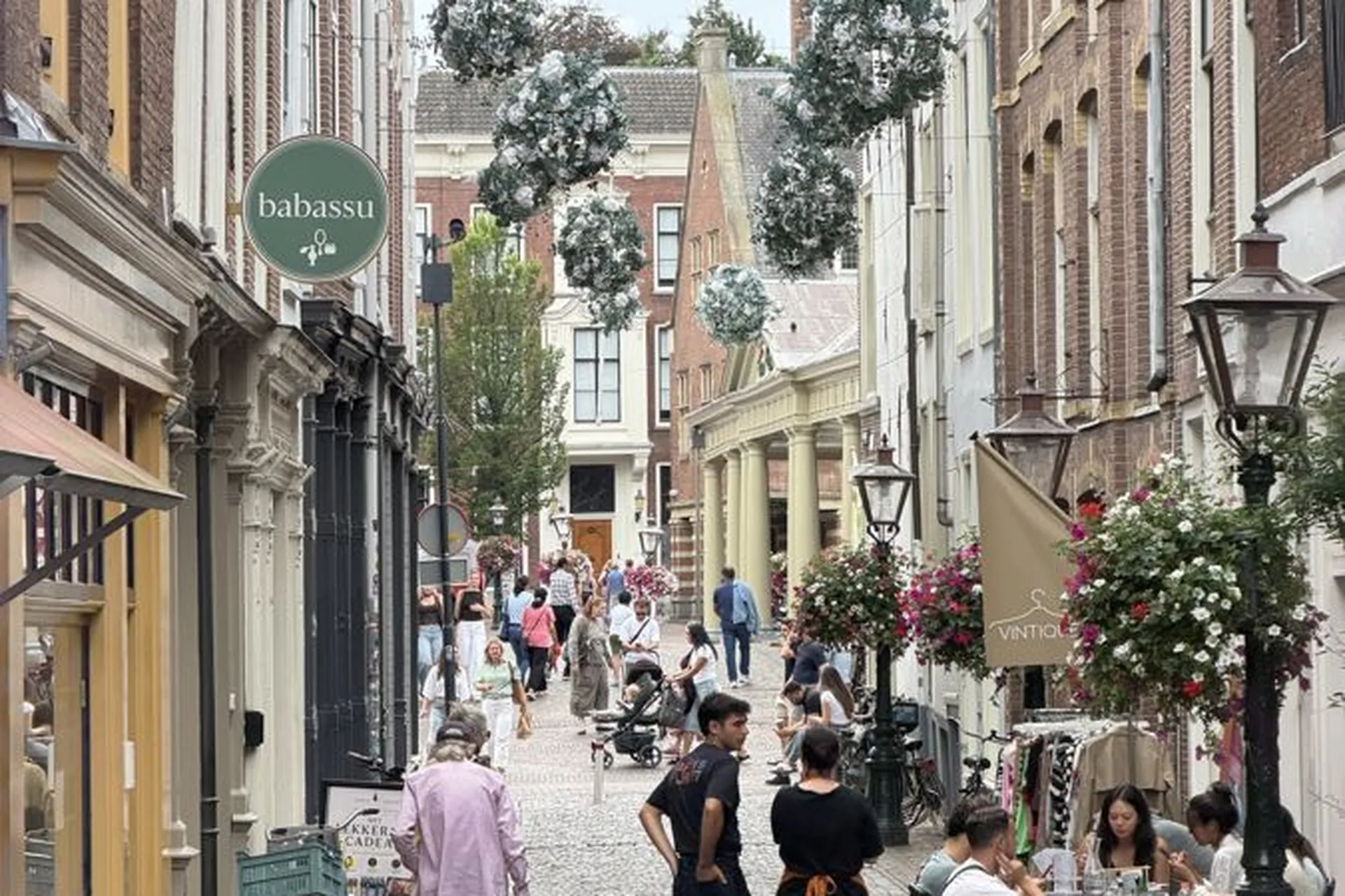 Belebte Einkaufsstraße in Leiden mit Blumenampeln und Terrassen